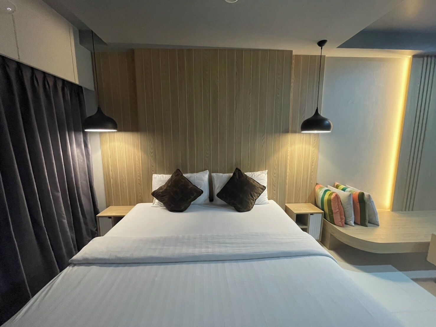 A hotel room with a large bed, two bedside tables, a wooden headboard, and a small seating area with cushions.