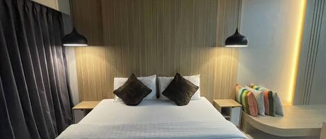 A hotel room with a large bed, two bedside tables, a wooden headboard, and a small seating area with cushions.