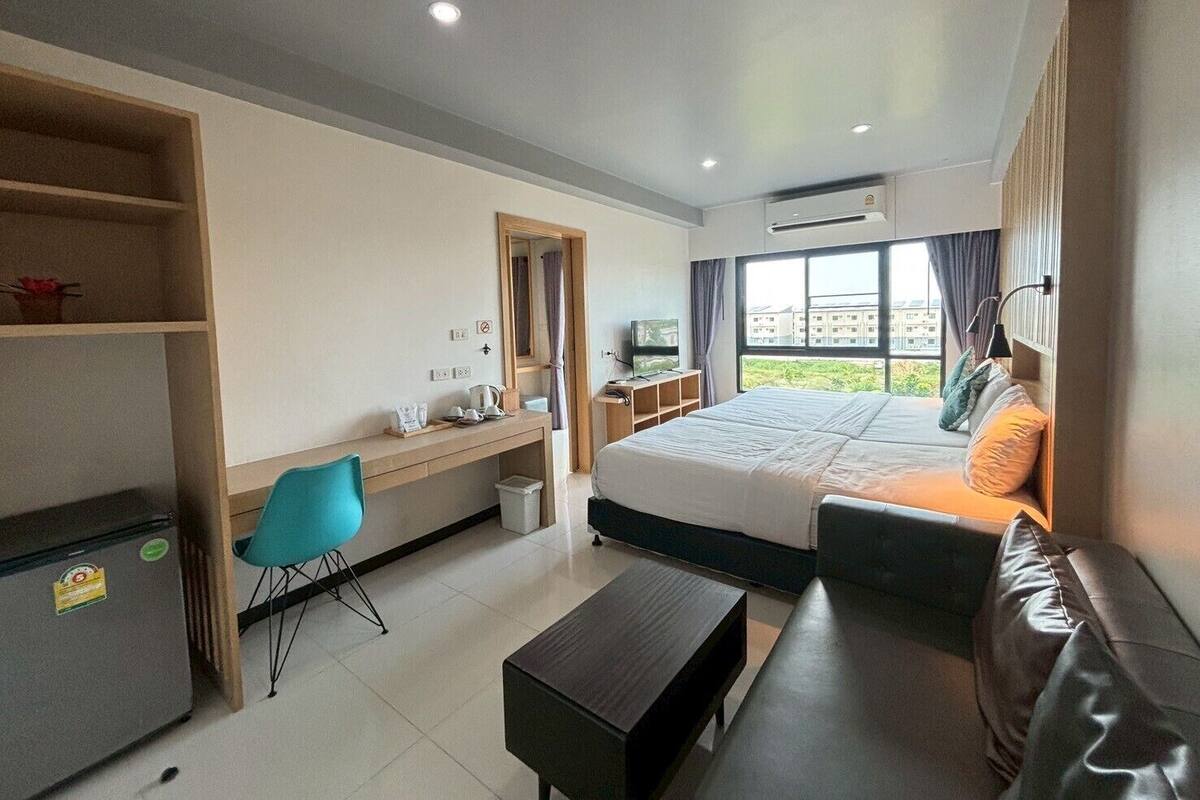 A hotel room with a bed, a desk, a chair, a small table, and a view of buildings through the window.