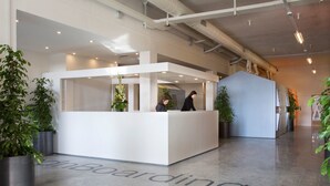 A modern reception area with a white reception desk, two staff members, and potted plants.