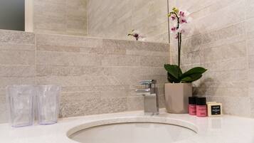 A bathroom with a sink, two clear glasses, a potted orchid, and two bottles of lotion.