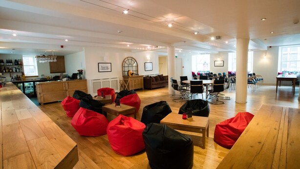 A spacious lounge area with wooden flooring, red bean bags, and a bar area in the background. - The Coffee House Hotel (Aberdeen)