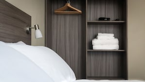 A neatly made bed with white linens, a wooden headboard, a bedside lamp, and a shelf with folded towels and a black object. - The Coffee House Hotel (Aberdeen)