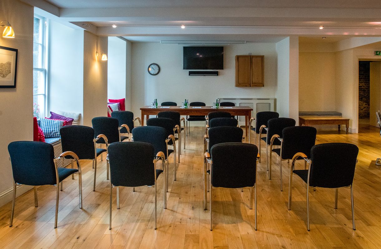 A conference room with a long table, chairs, a clock, and a TV on the wall.