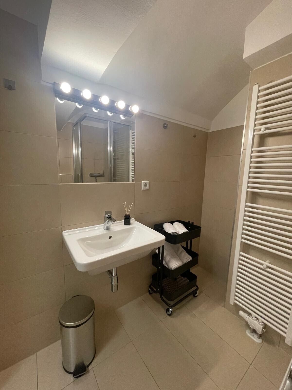 Une salle de bain avec un lavabo blanc, un miroir avec éclairage intégré, un porte-serviettes et une poubelle.