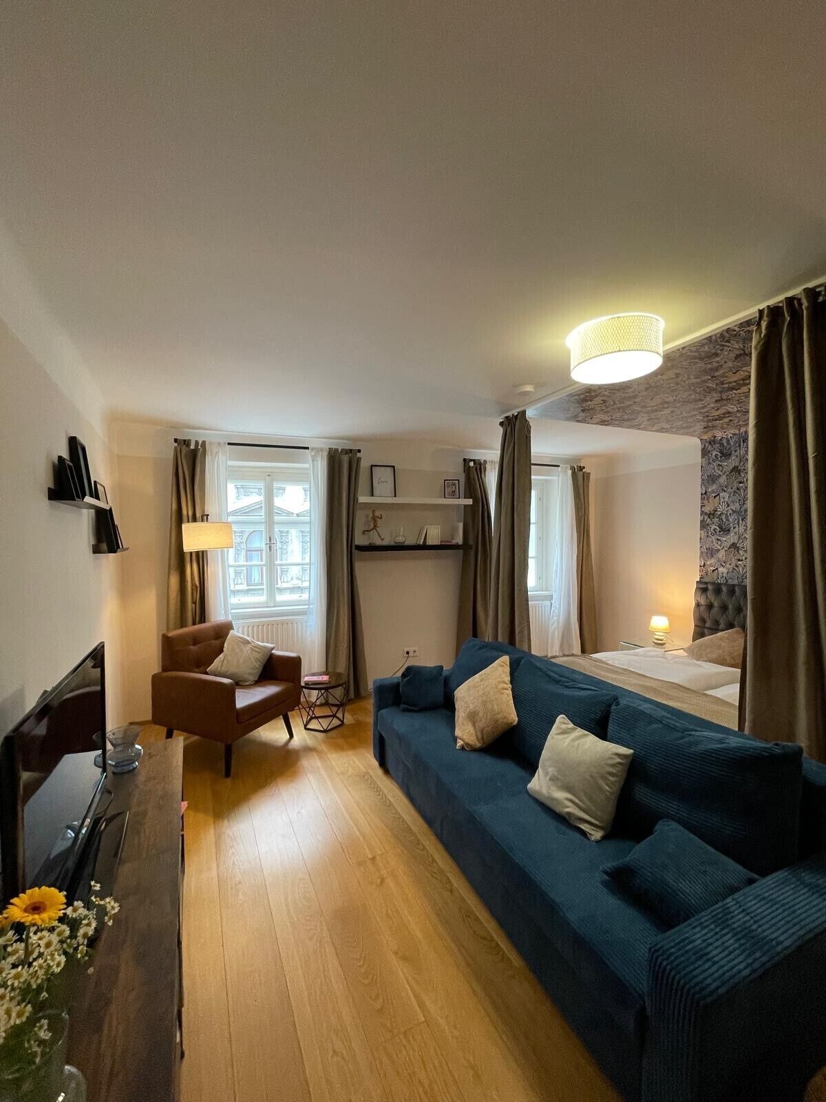 Ett mysigt hotellrum med en blå soffa, ett träbord, en liten fåtölj och en säng med en sänggavel.