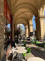 Um café ao ar livre com arcos elaborados, mesas redondas e cadeiras verdes.