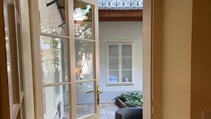 A doorway leading to an outdoor patio area with a wicker chair and a window with a sign. - KH Apartments (Vienna)