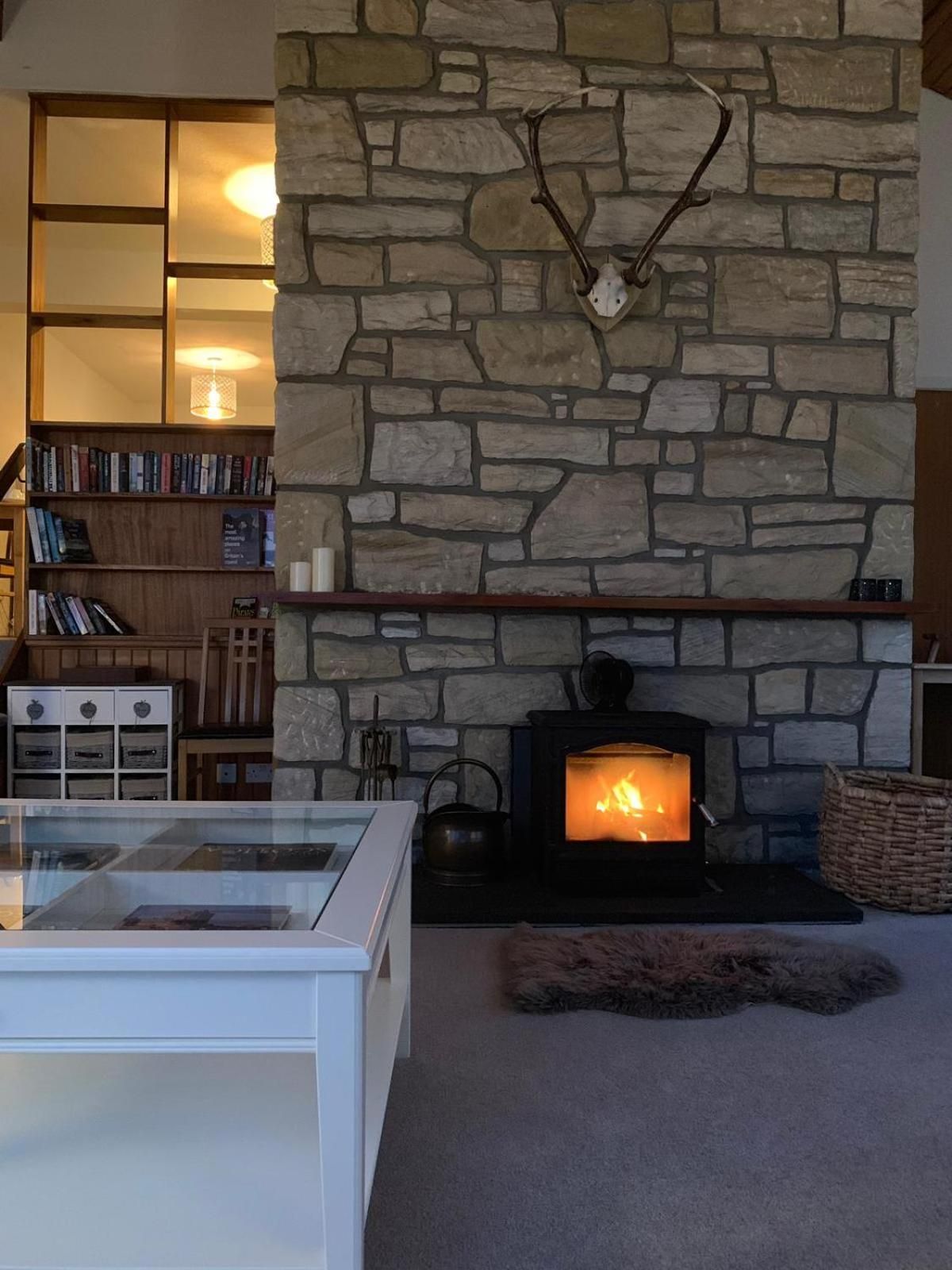 Una sala de estar acogedora con una chimenea de piedra, una mesa de centro de vidrio y una estantería.
