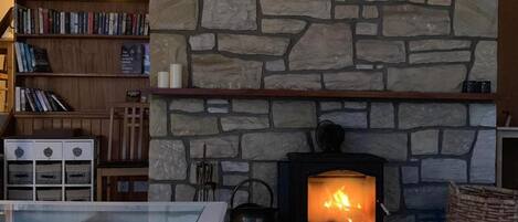 A cozy living room with a stone fireplace, a glass coffee table, and a bookshelf.