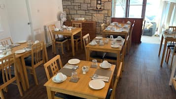 Un comedor con varias mesas y sillas de madera, decoración de pared de piedra y vistas amplias a través de grandes ventanales.