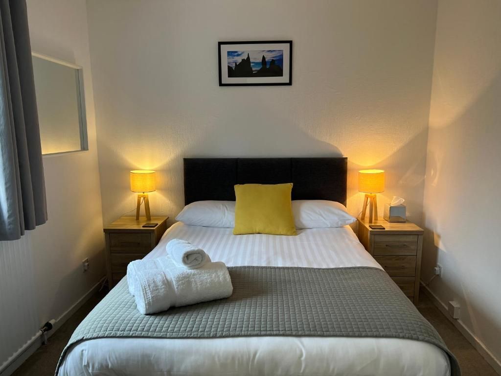 A hotel room with a bed, two bedside lamps, a picture on the wall, and a towel on the bed.