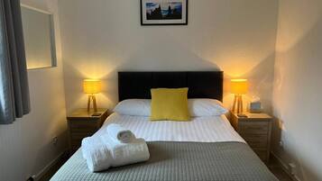 A hotel room with a bed, two bedside lamps, a picture on the wall, and a towel on the bed.