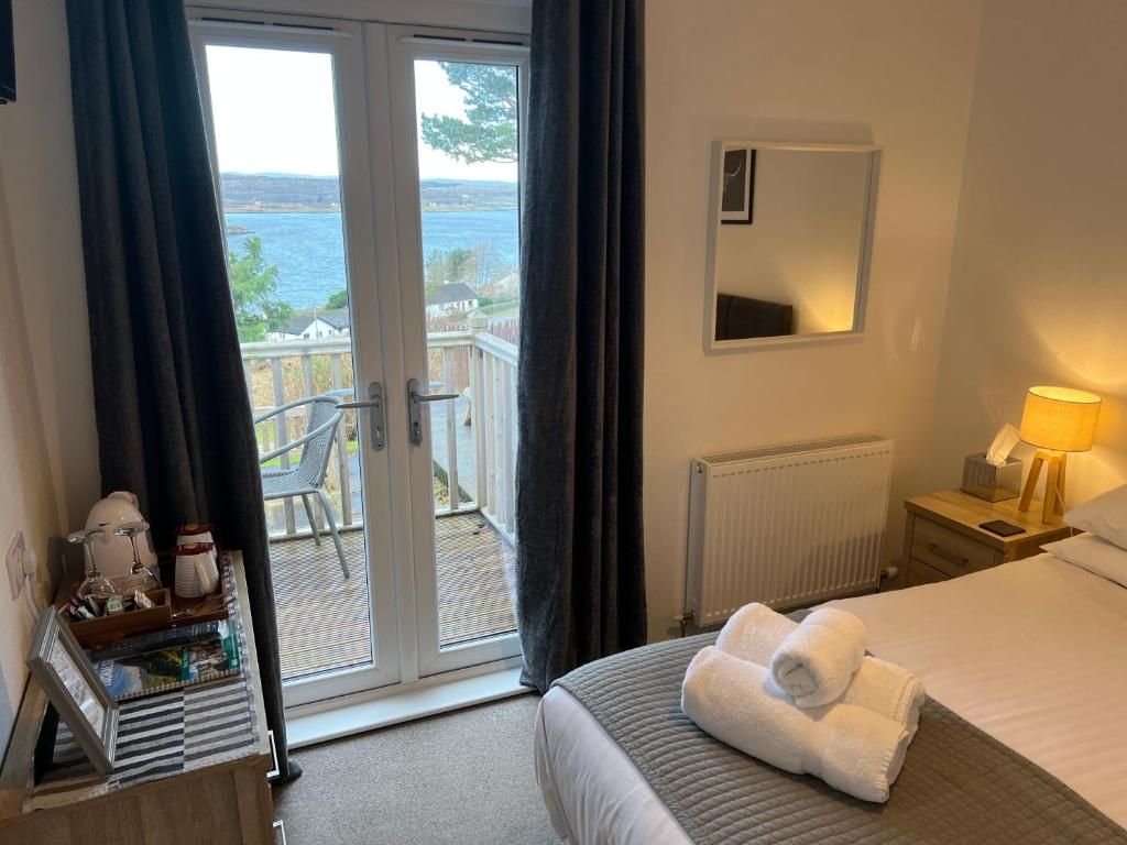 A hotel room with a bed, a bedside table with a lamp, a window with curtains, and a view of the sea.