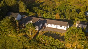 Vue aérienne d’un bâtiment blanc doté d’un toit en pente, entouré d’une forêt dense.