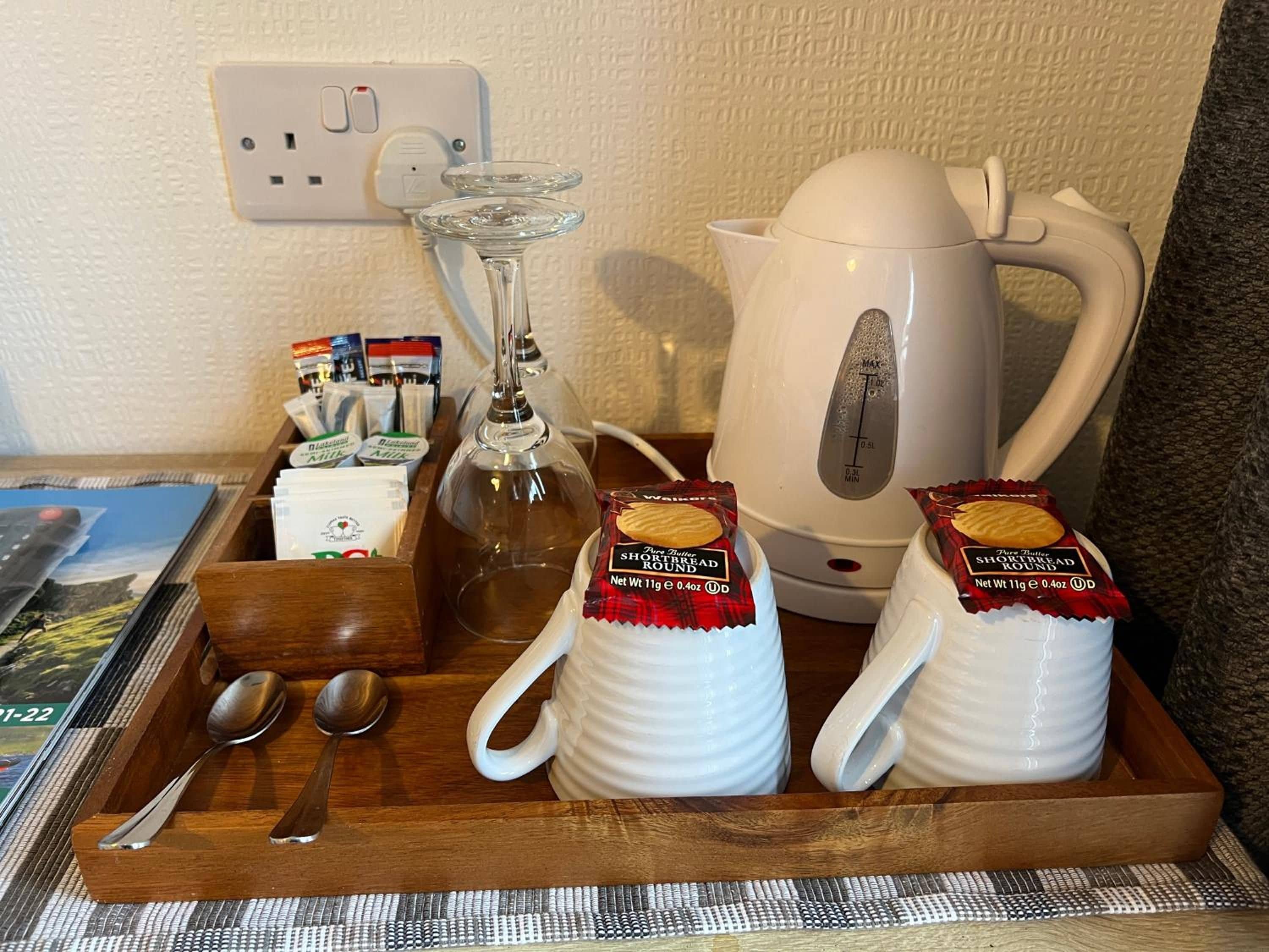 A tray with a teapot, two mugs, a glass, and a wooden tray with utensils.