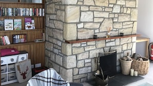 Un salon chaleureux avec une cheminée en pierre, une bibliothèque remplie de livres et un coin salon confortable.
