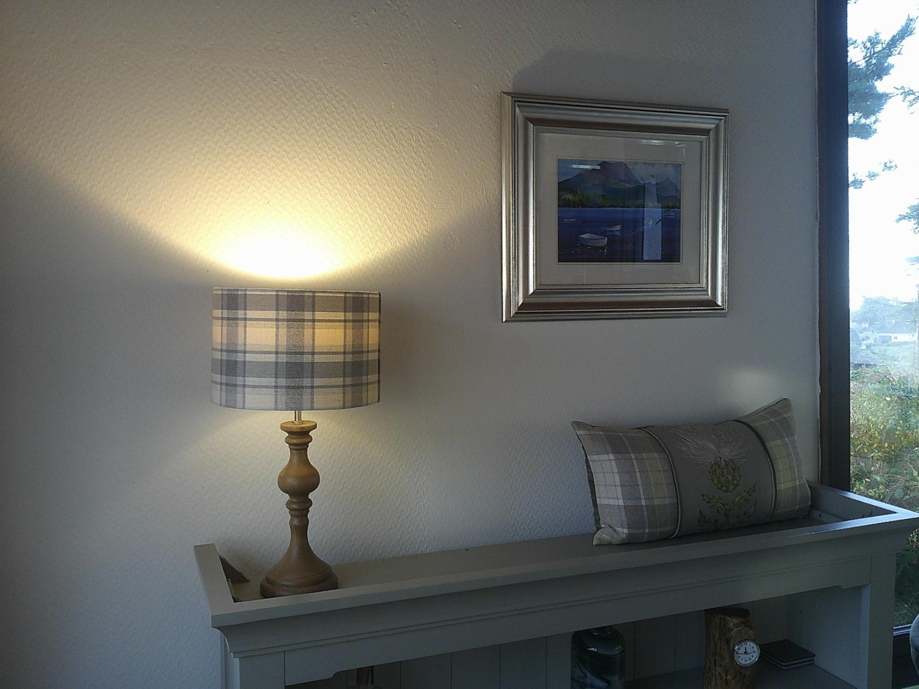Une pièce avec une lampe posée sur une console blanche, un tableau encadré au mur et une fenêtre donnant sur un paysage.