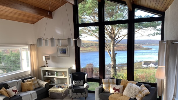 Un salon spacieux doté d’une grande fenêtre offrant une vue panoramique sur un lac et une forêt.
