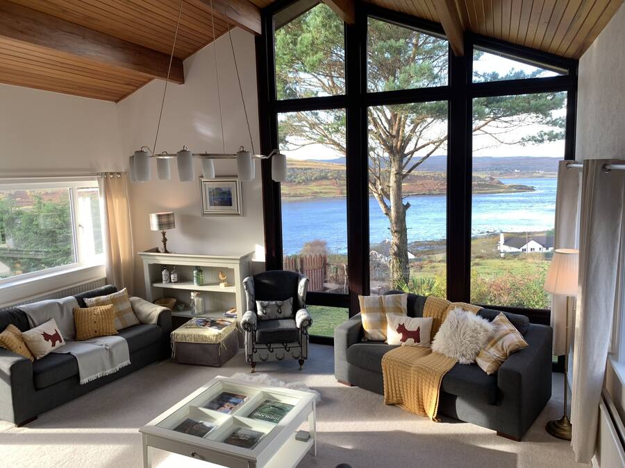 Un salon spacieux doté d’une grande fenêtre offrant une vue panoramique sur un lac et une forêt.