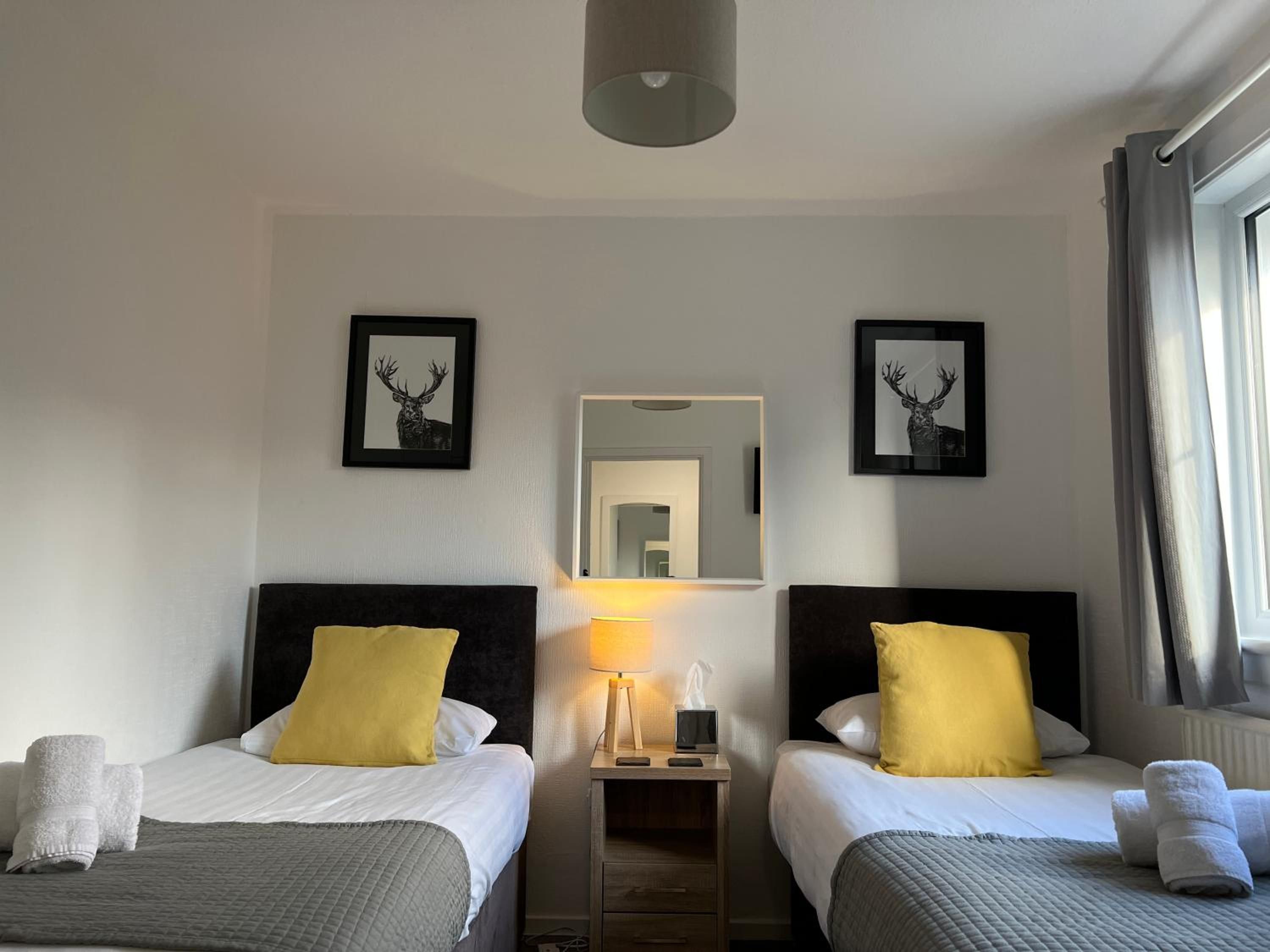 A hotel room with two beds, each with a headboard, a bedside table with a lamp, and towels.