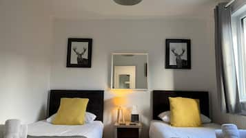 A hotel room with two beds, each with a headboard, a bedside table with a lamp, and towels.