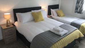 Une chambre d’hôtel avec deux lits, chacun étant équipé de draps blancs et d’un oreiller jaune. On y trouve une table de chevet avec une lampe et un téléphone.