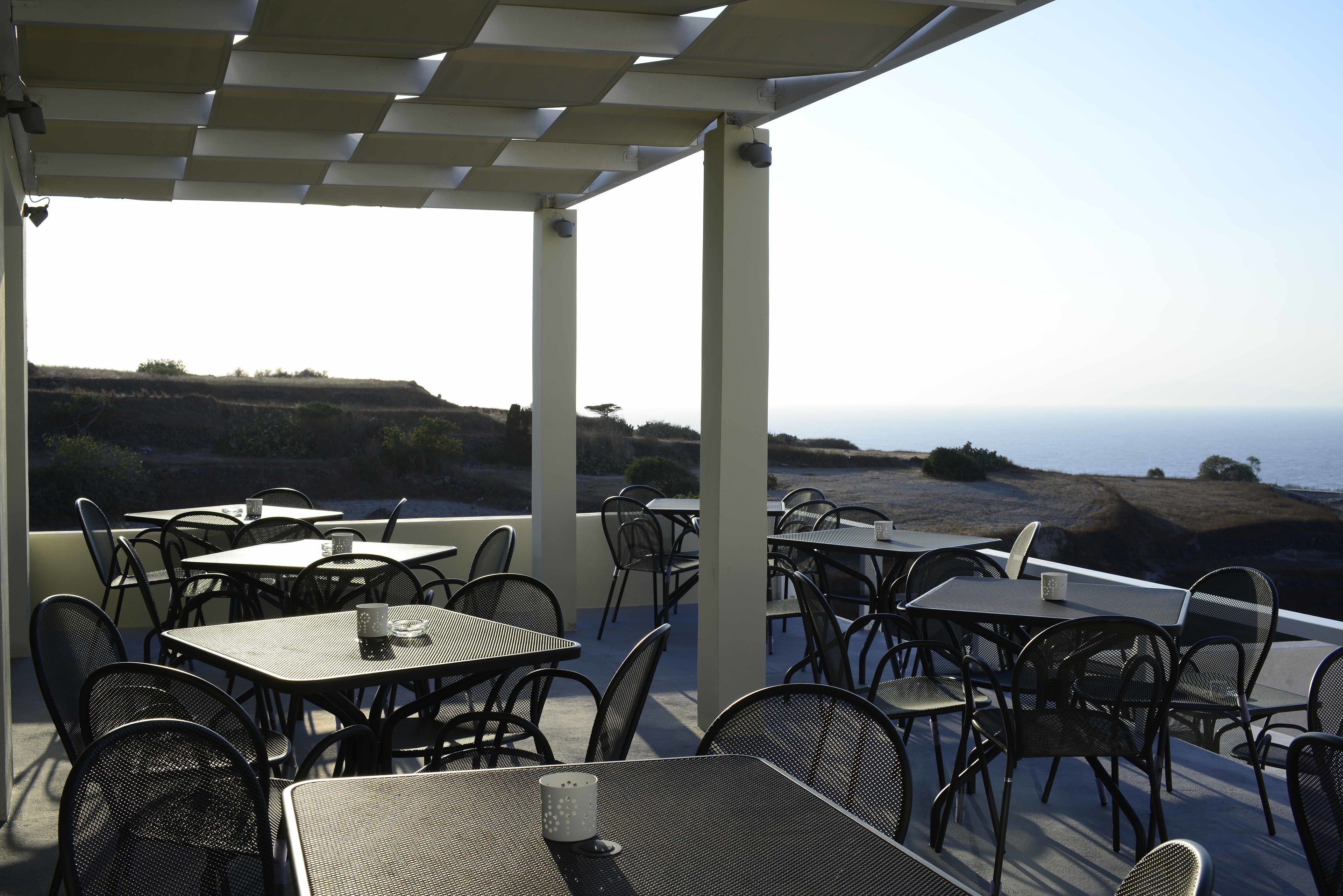 An outdoor patio with tables and chairs, overlooking a coastal landscape.