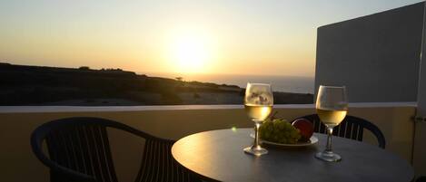 A table with two glasses of white wine and a plate of grapes and an apple, overlooking a sunset over the sea.