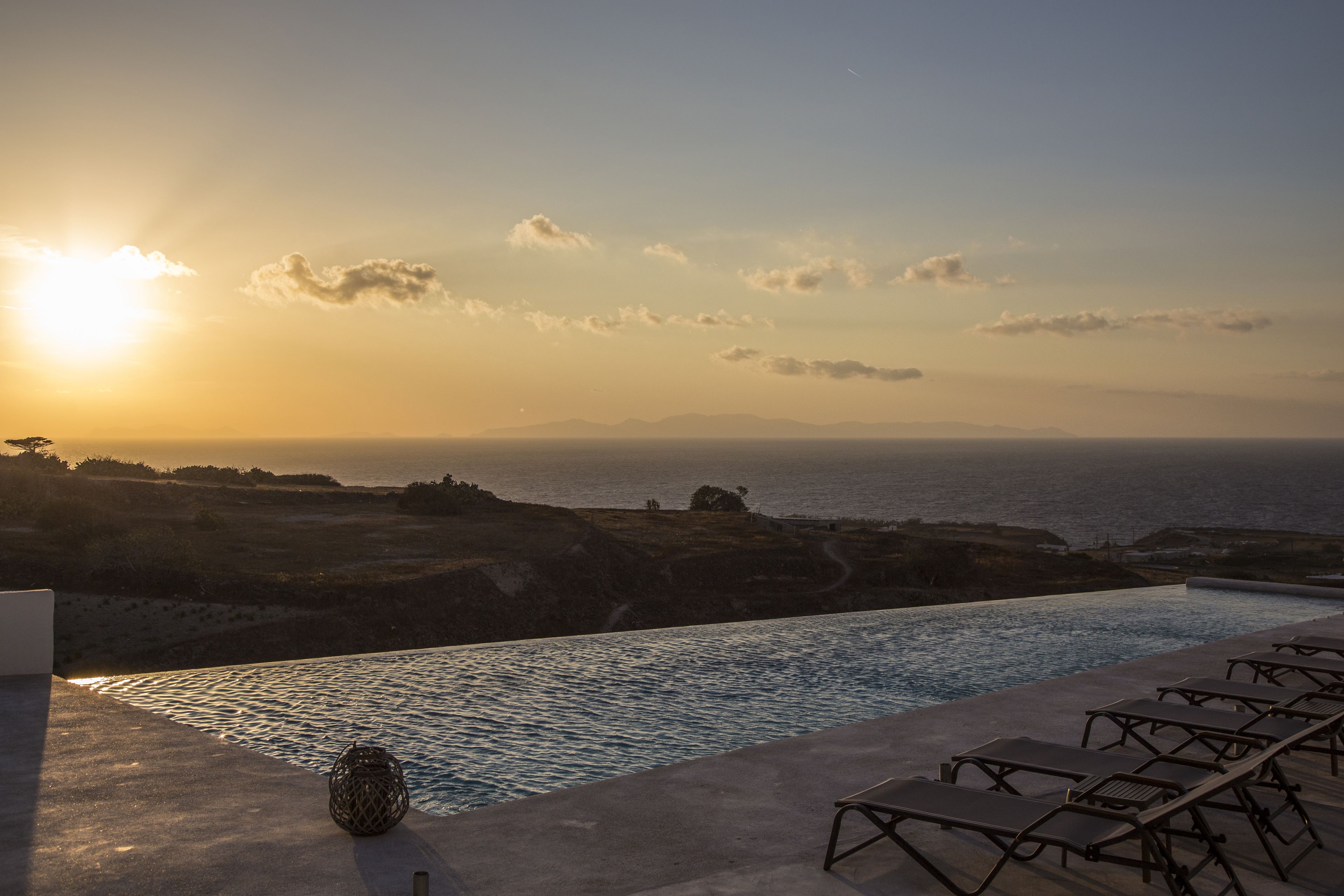 An infinity pool with lounge chairs and a view of the ocean at sunset.
