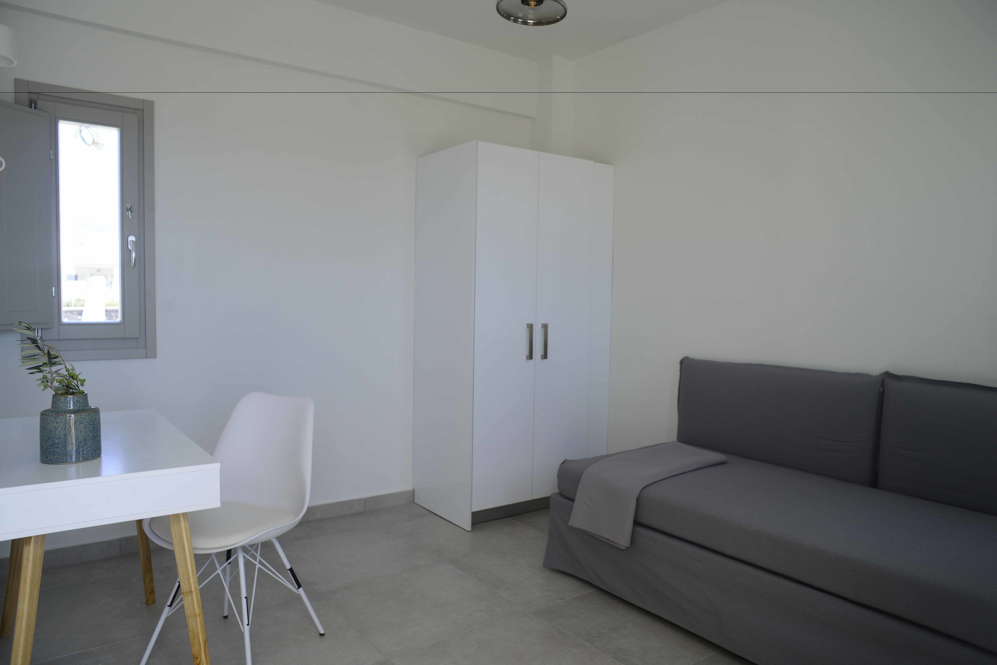 Une pièce moderne et minimaliste, avec une table blanche, une chaise blanche, un canapé gris et une grande armoire.
