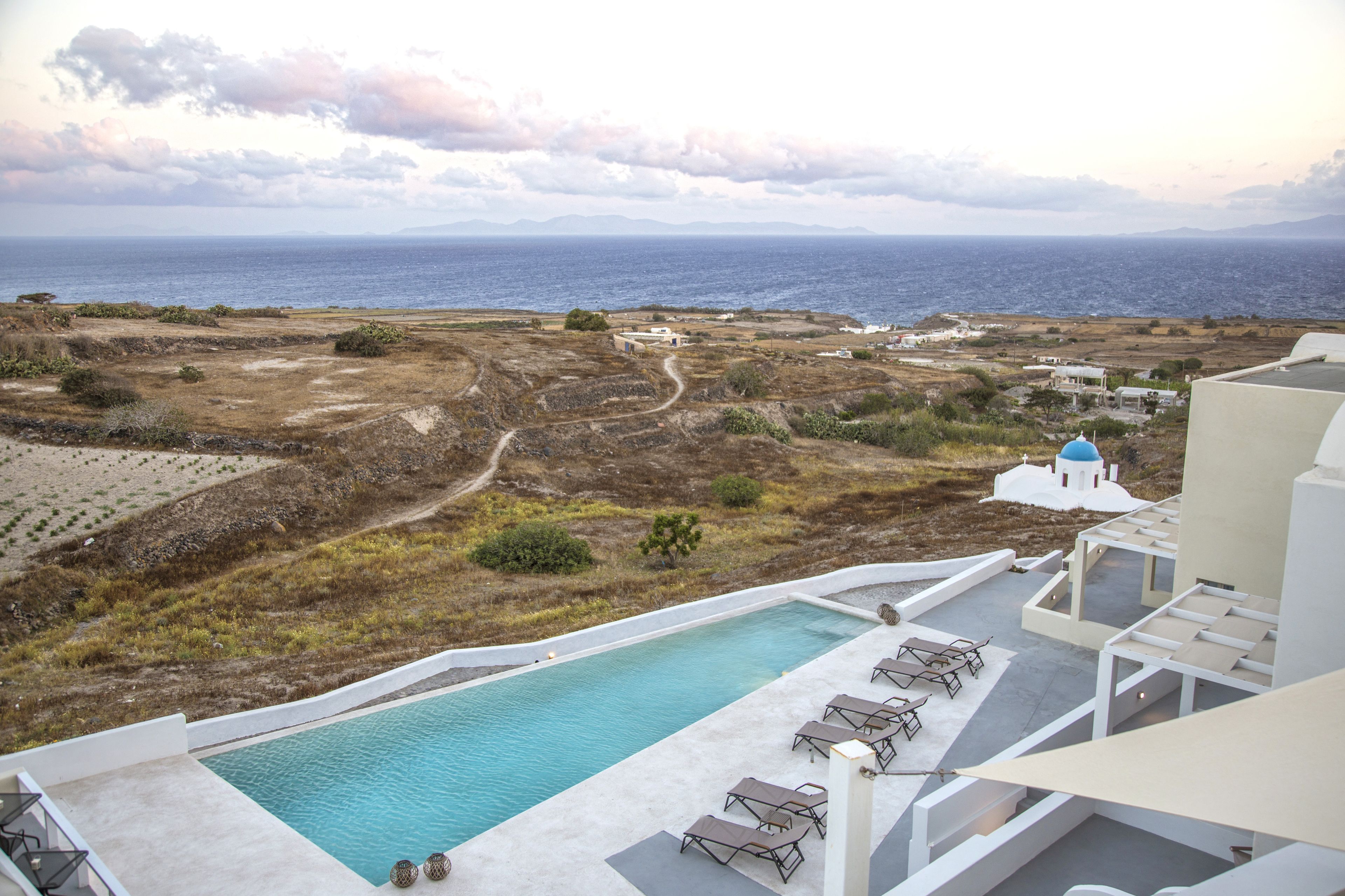 A pool area with a view of the sea, a path, and some buildings in the background.