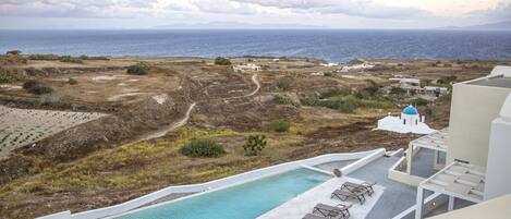 A pool area with a view of the sea, a path, and some buildings in the background.