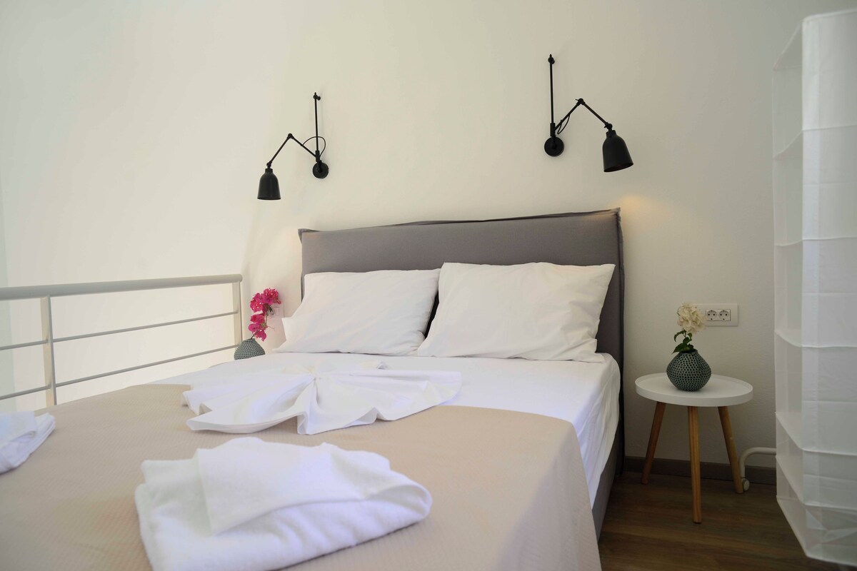 A neatly made bed with white linens, a grey headboard, and two wall-mounted lamps.