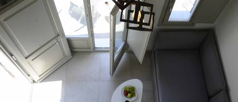 Una cocina compacta con comedor, una mesa blanca con un bol de fruta y bebidas, y un sofá gris.
