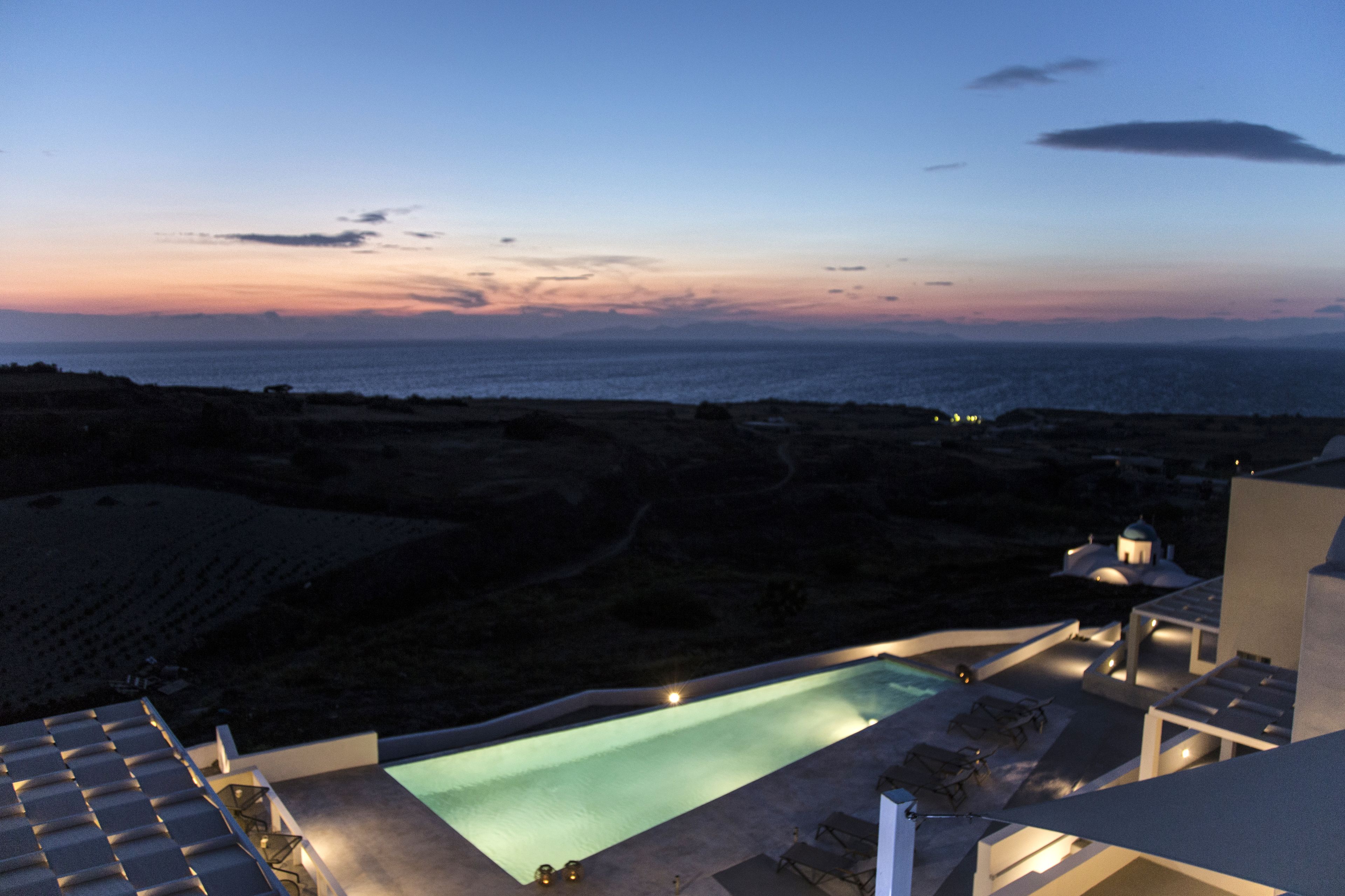 A pool area with lounge chairs and a view of the sea at dusk.