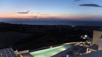 Zona de piscina con sillones de descanso y vista al mar al atardecer.