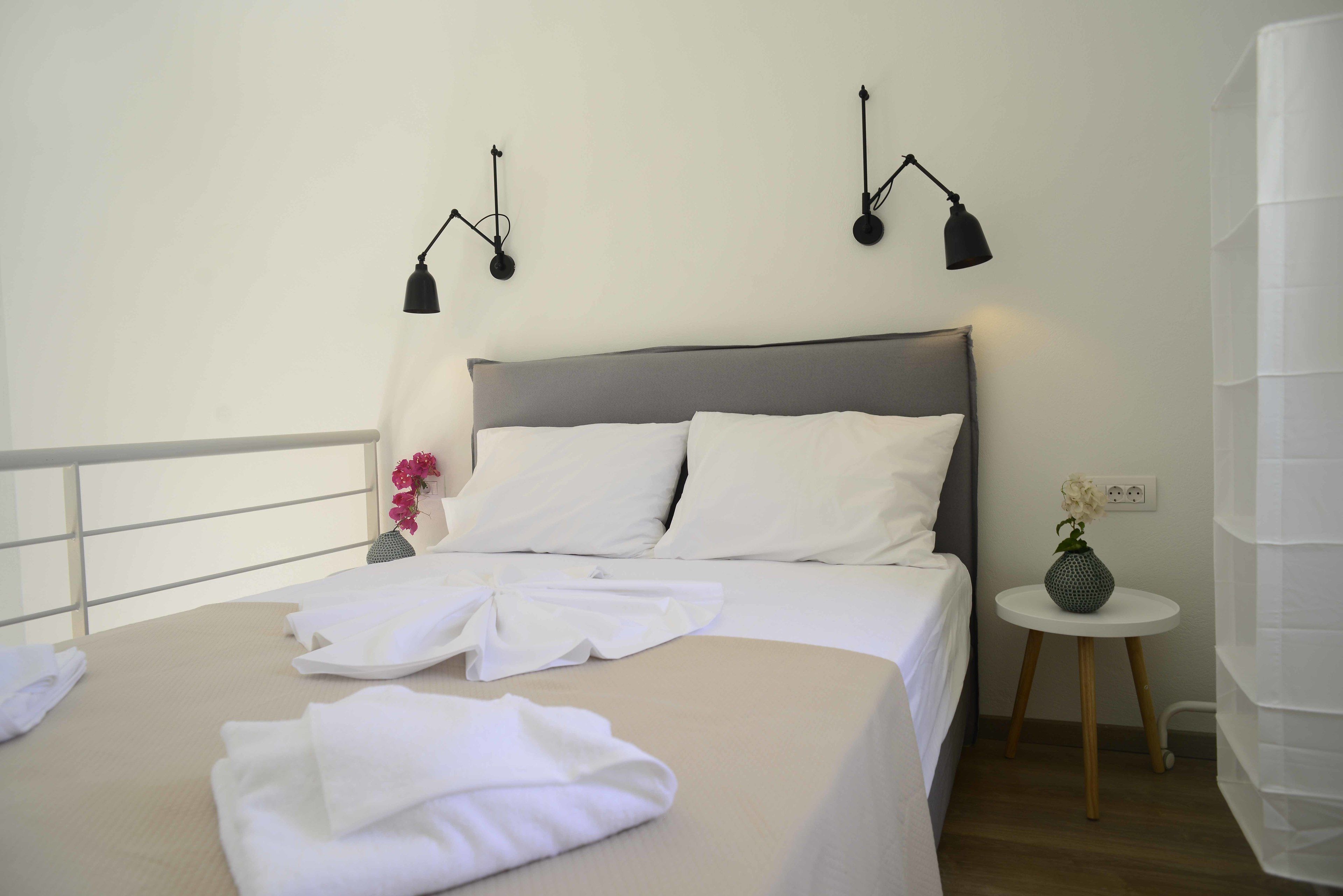 A neatly made bed with white linens, a grey headboard, and two wall-mounted lamps.