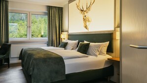 Ein Hotelzimmer mit einem großen Bett, Blick auf Grün durch das Fenster und einem Hirschbild an der Wand.