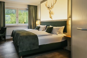 A hotel room with a large bed, a view of greenery through the window, and a deer head artwork on the wall.