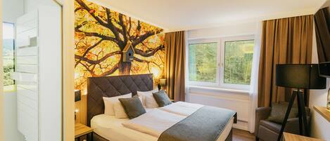 A bedroom with a large bed, a window with curtains, a bedside table, a lamp, and a television.