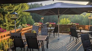 Eine Terrasse im Freien mit Tischen, Stühlen und einem großen Sonnenschirm, sowie einem hölzernen Geländer.