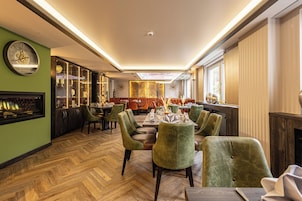 A dining area with a herringbone wood floor, green upholstered chairs, and a central table set for a meal.