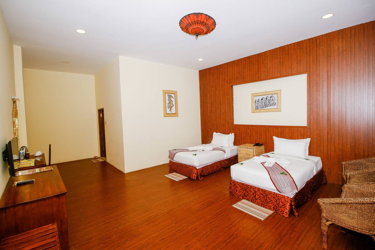 A hotel room with two beds, wooden paneling, a desk with a telephone, and two framed pictures on the wall.