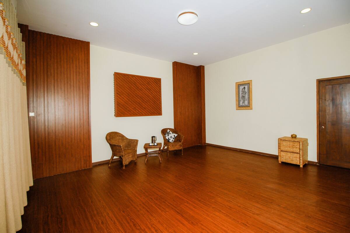 A room with wooden flooring, two wicker chairs, a small table, a framed picture on the wall, and a wooden door.