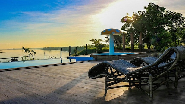 Een houten terras met ligstoelen en een zwembad, met uitzicht op een waterpartij en een zonsondergang.