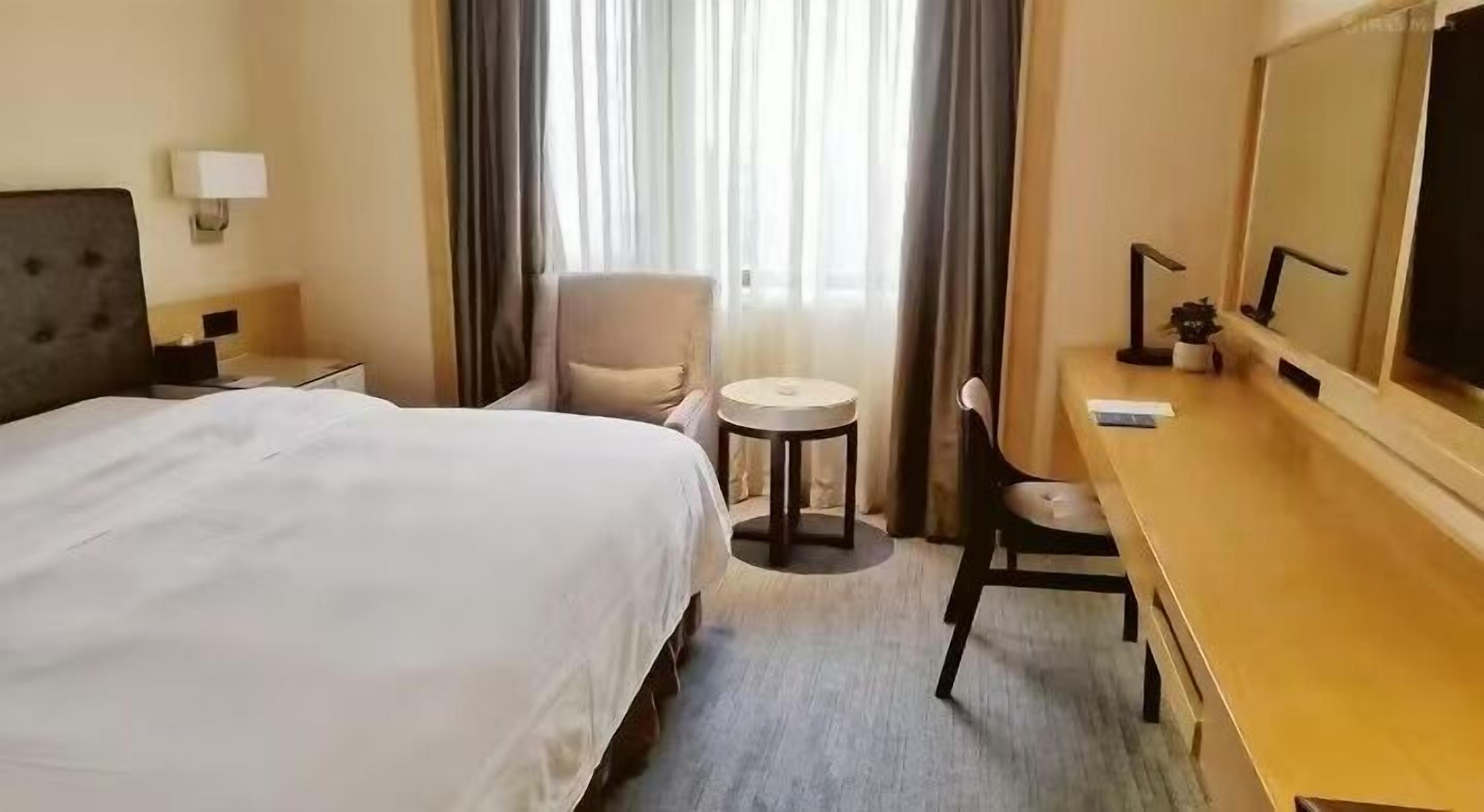 Habitación de hotel con cama, escritorio, silla, mesa redonda, lámpara y un espejo grande.