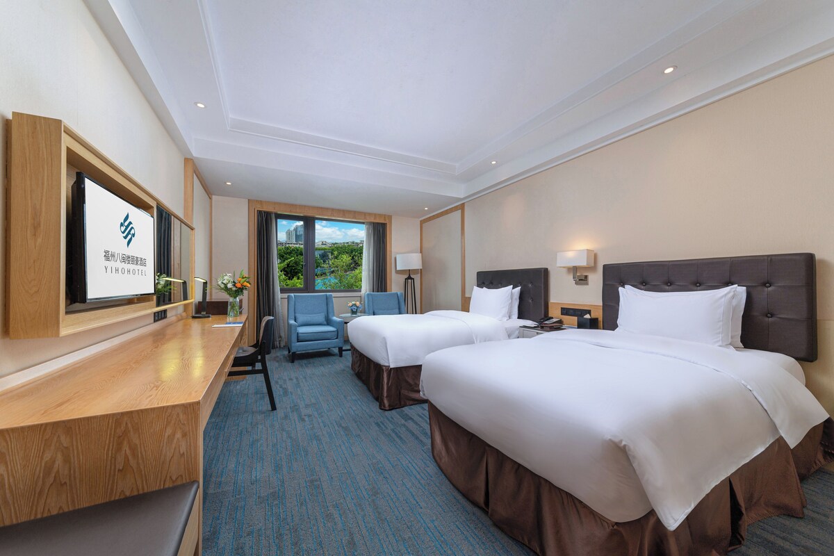 A hotel room with two beds, a desk, a chair, and a TV.