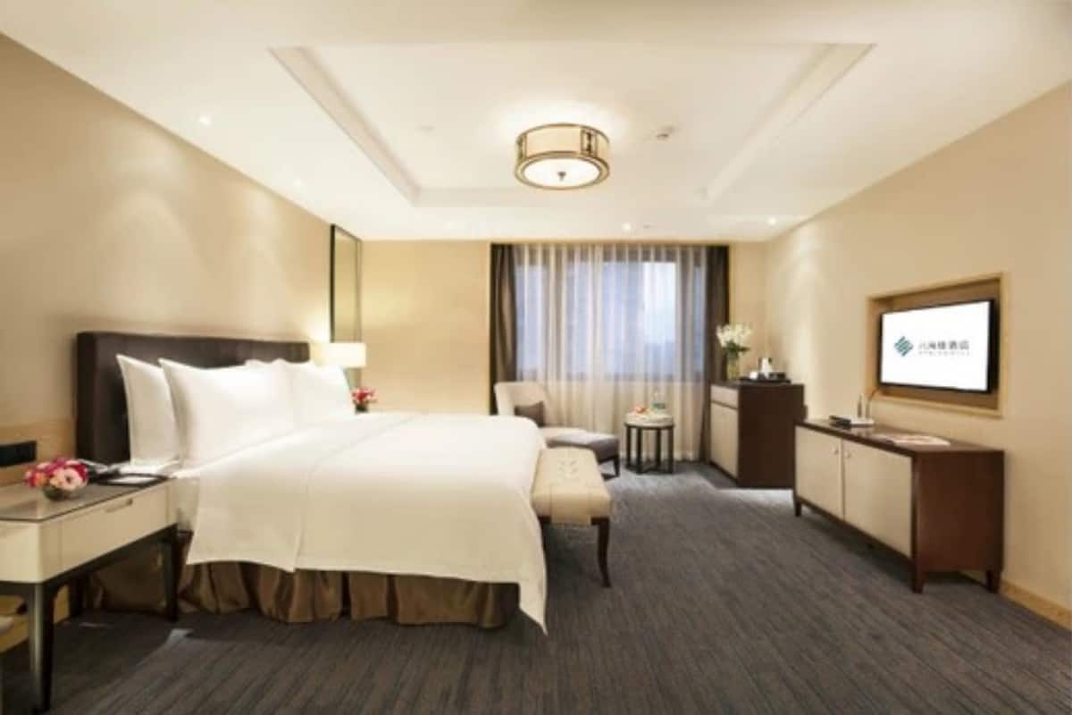 A hotel room with a large bed, a desk, a chair, a small table, a TV, and a window with curtains.