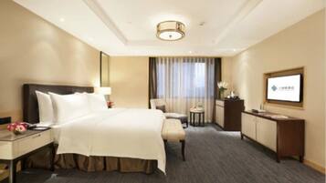 A hotel room with a large bed, a desk, a chair, a small table, a TV, and a window with curtains.